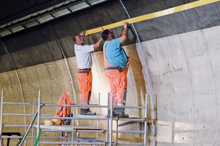 Deux ouvriers du tunnel sur un châssis de chantier en train d'appliquer du ruban adhésif
