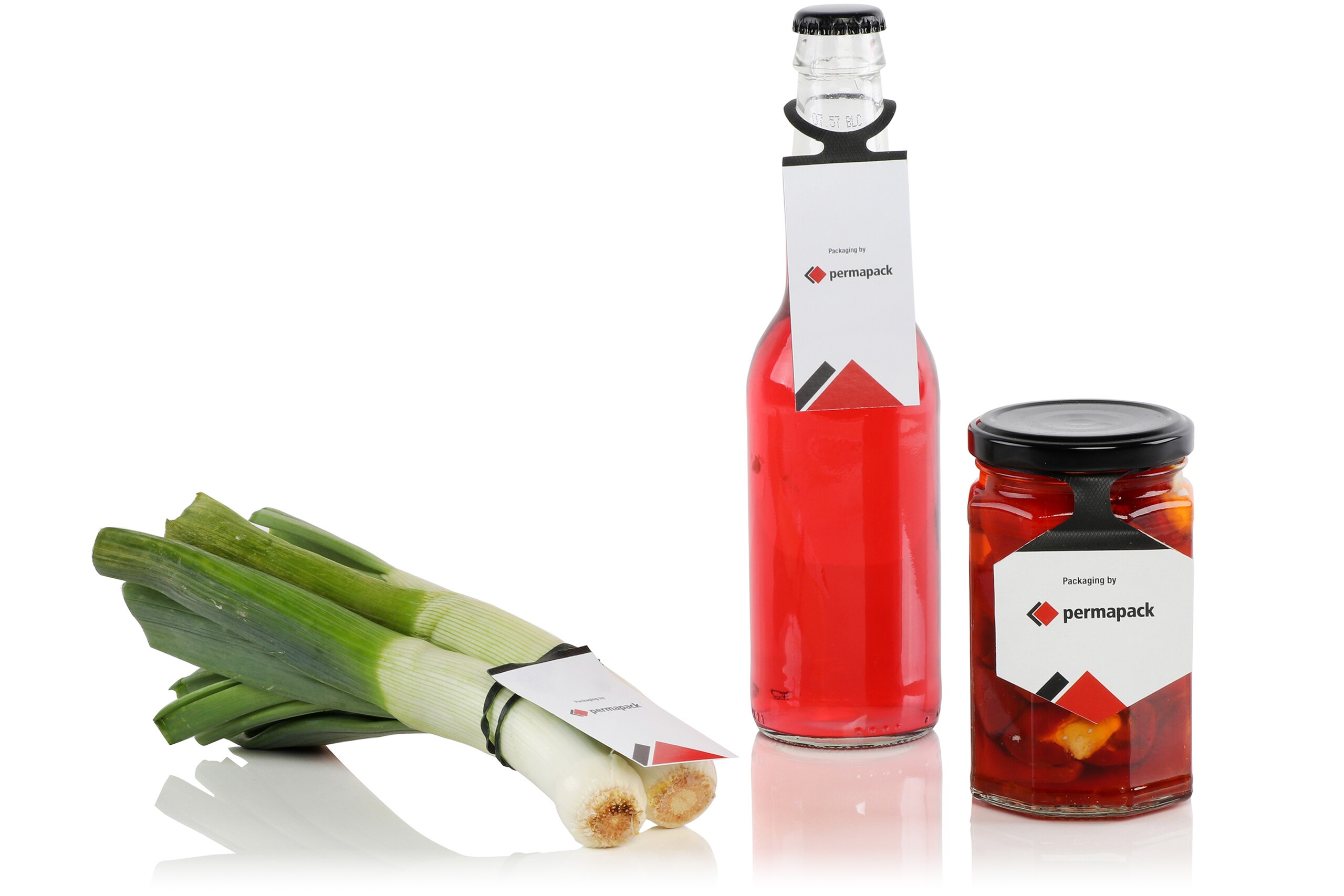 Zwei Lauchstängel, eine Glasflasche mit roter Flüssigkeit und ein rotes Schraubverschlussglas mit Elastitag-Etiketten.