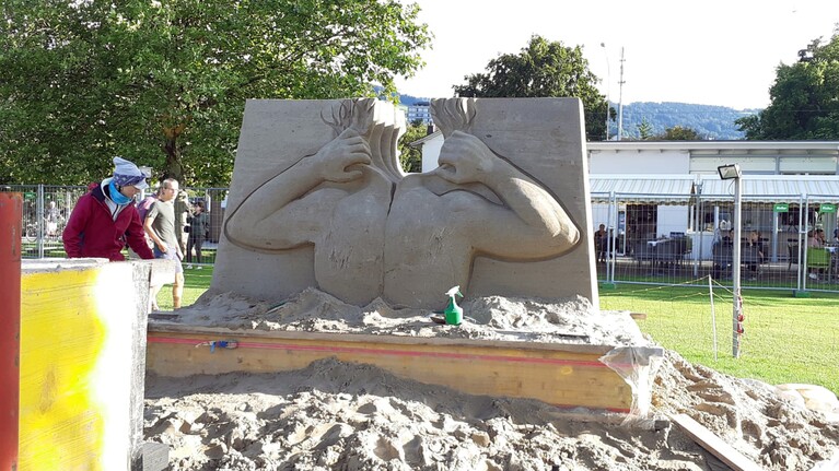 Eine Frau bearbeitet eine Sandskulptur am Bodensee
