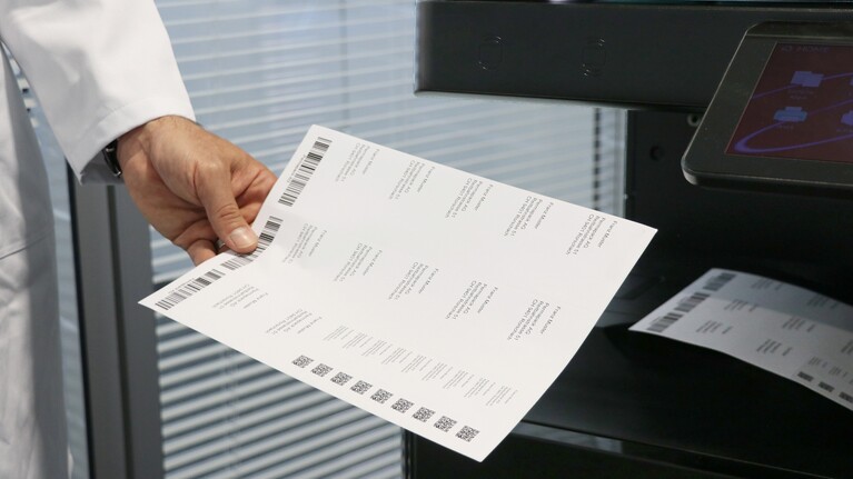 Mann nimmt bedrucktes Etikettenblatt aus dem Drucker.