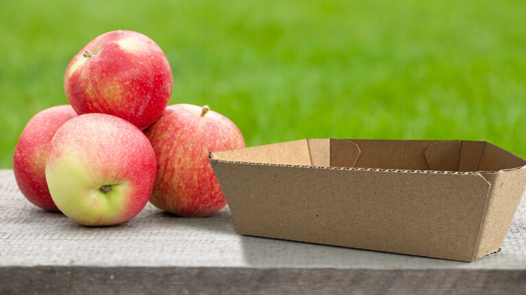 Quatre pommes à côté d'une barquette en carton.