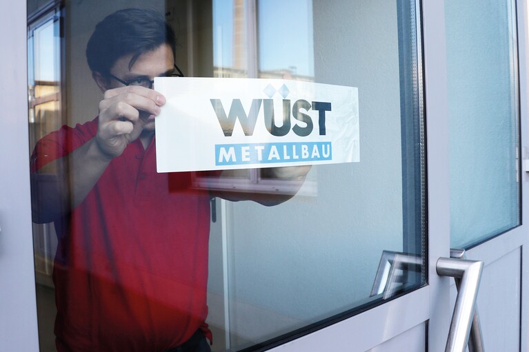 Un homme colle une étiquette de fenêtre sur une vitre de porte.