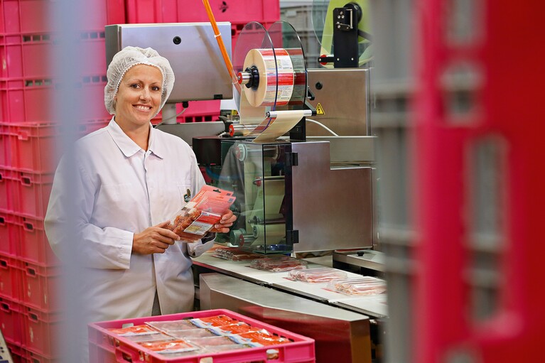 Femme travaillant sur une machine d'emballage dans une usine de transformation de viande.