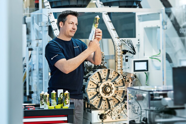 Un homme se tient devant une machine de fabrication de tubes et contrôle un tube terminé.