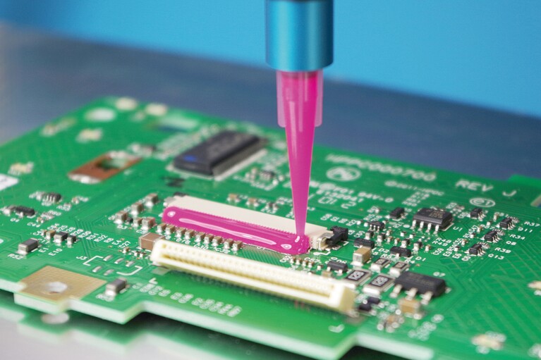 Une chenille de colle rose sur un circuit imprimé vert.