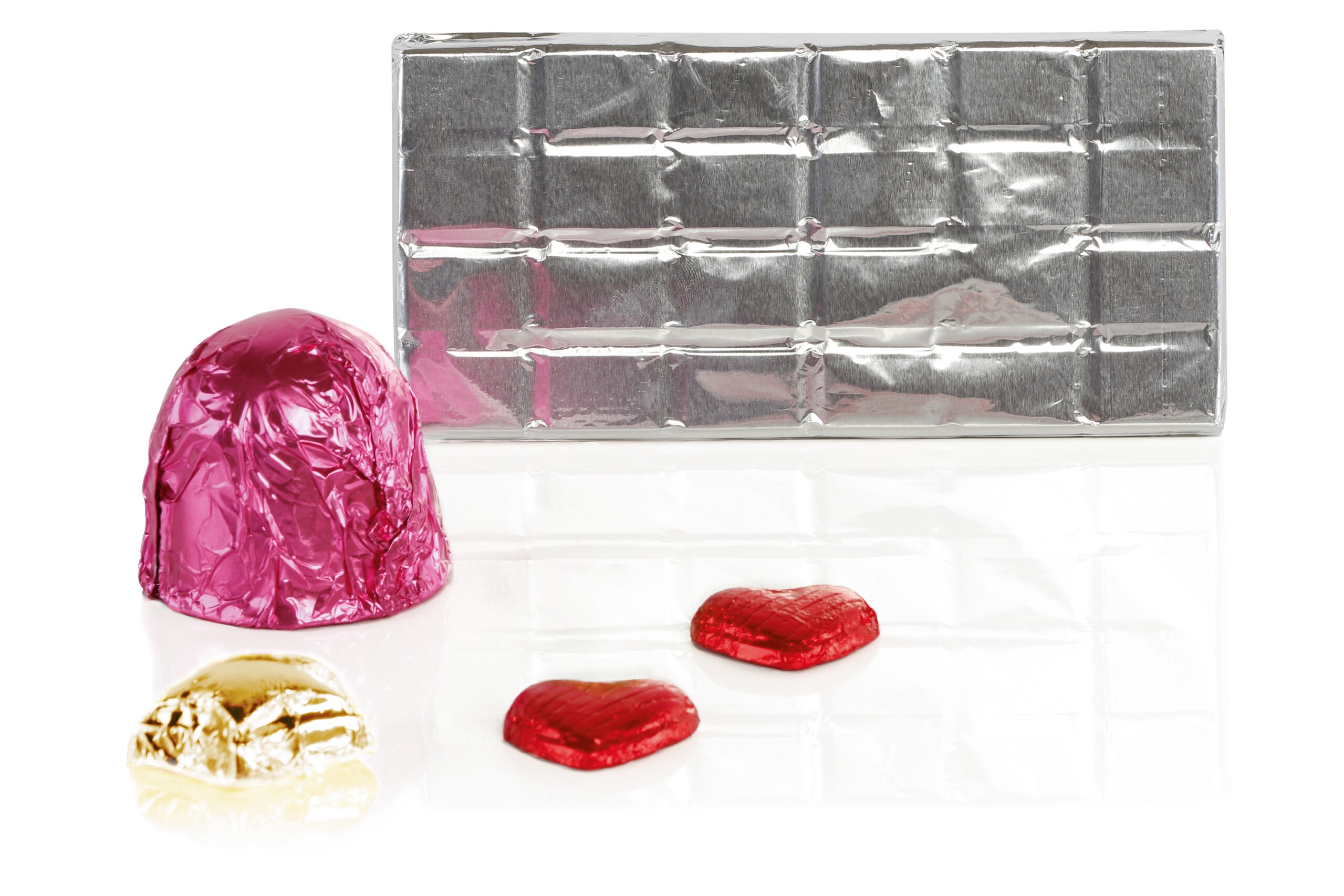 Un baiser au chocolat dans une feuille d'aluminium rose, deux petits cœurs en chocolat dans une feuille d'aluminium rouge, une petite étoile dans une feuille d'aluminium jaune et une tablette de chocolat enveloppée dans une feuille d'aluminium