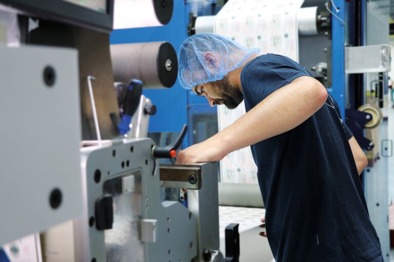 Mann prüft auf der Druckmaschine die Druckqualität von Etiketten